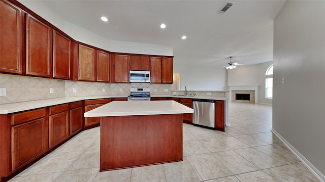 kitchen with decorative backsplash, a fireplace, stainless steel appliances, a center island, and ceiling fan