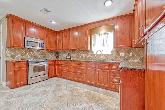 kitchen featuring appliances with stainless steel finishes, decorative backsplash, dark stone counters, and sink