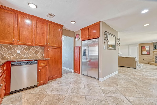 kitchen with a fireplace, stone countertops, light tile patterned floors, tasteful backsplash, and stainless steel appliances