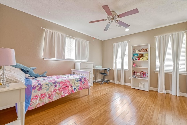 bedroom with a textured ceiling, ceiling fan, and light hardwood / wood-style floors