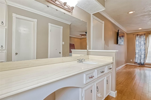 kitchen with light wood-type flooring, ornamental molding, sink, ceiling fan, and white cabinets