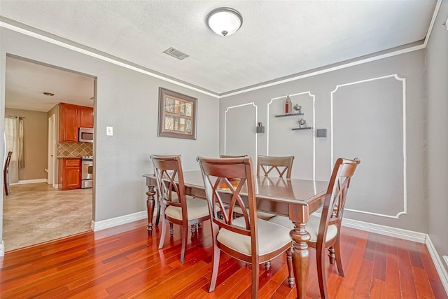 dining room featuring wood-type flooring, a textured ceiling, and ornamental molding