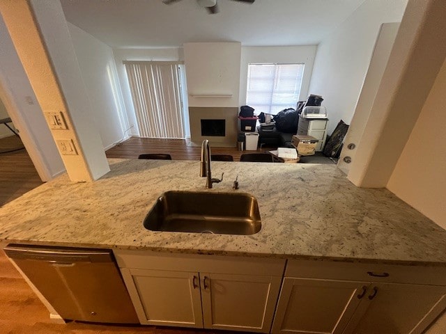 kitchen featuring dishwasher, light stone counters, open floor plan, a fireplace, and a sink