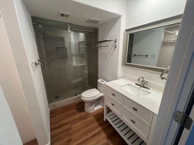 bathroom with wood-type flooring, vanity, toilet, and a shower with shower door