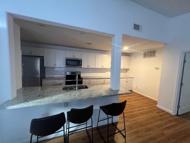 kitchen with kitchen peninsula, white cabinetry, a kitchen breakfast bar, appliances with stainless steel finishes, and dark hardwood / wood-style flooring