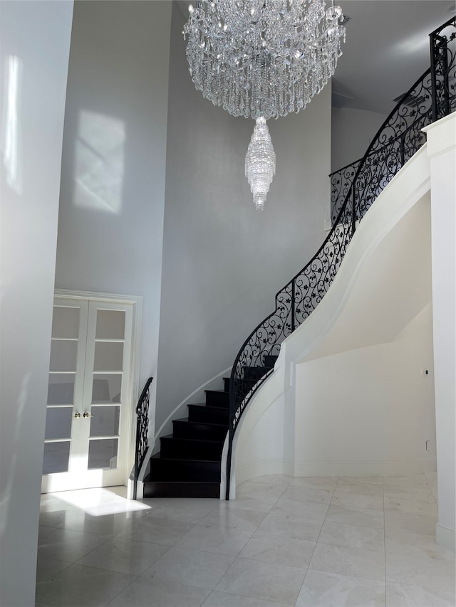 staircase with a high ceiling, a notable chandelier, and french doors