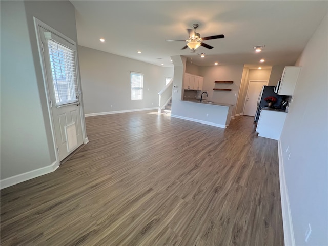 unfurnished living room with ceiling fan, sink, and dark wood-type flooring