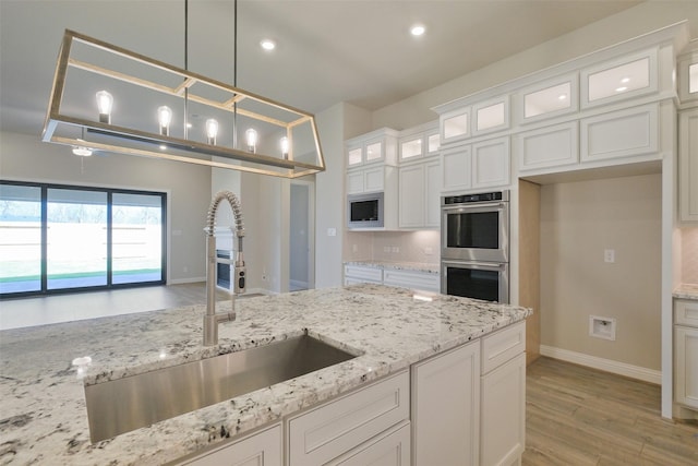 9715 Hunters Run Dr, Missouri City, TX 77459 - kitchen with light wood finished floors, appliances with stainless steel finishes, hanging light fixtures, white cabinetry, and a sink