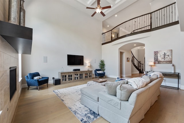 living room with a towering ceiling, a tile fireplace, beam ceiling, ceiling fan, and hardwood / wood-style flooring