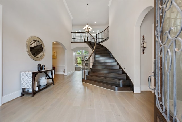 entryway featuring ornamental molding, a notable chandelier, a towering ceiling, and light hardwood / wood-style floors