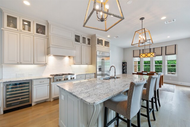 kitchen with wine cooler, a kitchen island with sink, white cabinets, an inviting chandelier, and appliances with stainless steel finishes