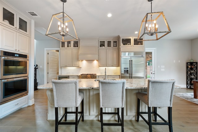 kitchen with stainless steel appliances, a chandelier, a center island with sink, and hardwood / wood-style floors