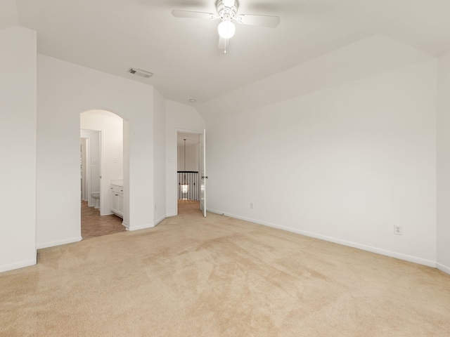 unfurnished bedroom featuring connected bathroom, light colored carpet, vaulted ceiling, and ceiling fan