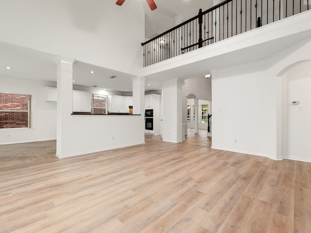 unfurnished living room featuring ceiling fan, light hardwood / wood-style flooring, a healthy amount of sunlight, and a high ceiling