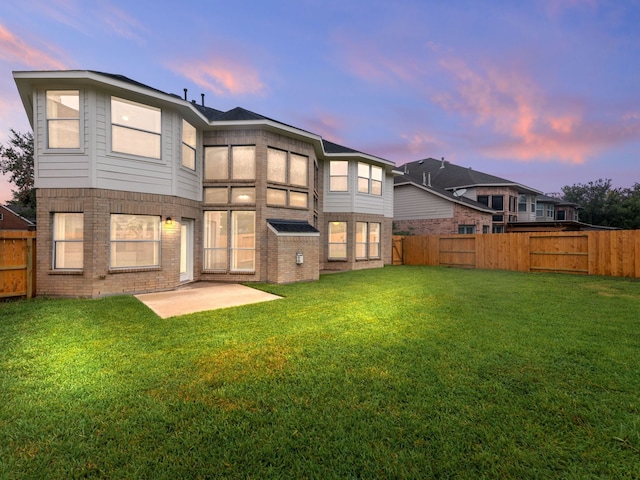 back house at dusk featuring a yard and a patio