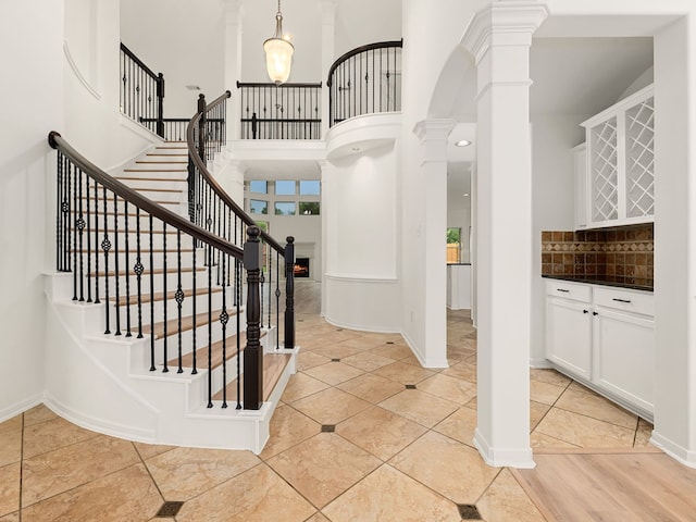 stairs with wood-type flooring, a towering ceiling, and ornate columns