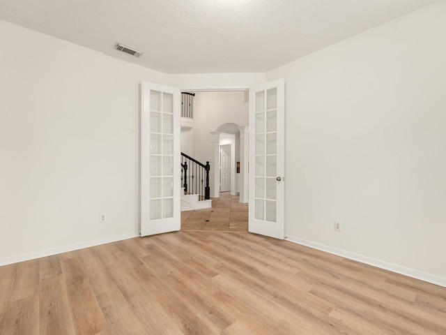 empty room featuring french doors, a textured ceiling, and light wood-type flooring