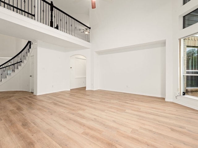 unfurnished living room with a towering ceiling, light hardwood / wood-style floors, and ceiling fan