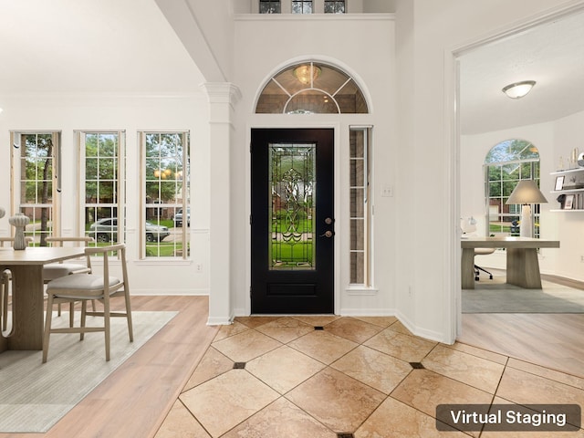 foyer with a healthy amount of sunlight, wood-type flooring, crown molding, and ornate columns