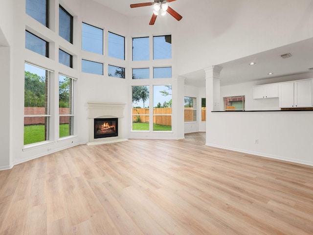 unfurnished living room featuring a towering ceiling, light hardwood / wood-style flooring, and ceiling fan