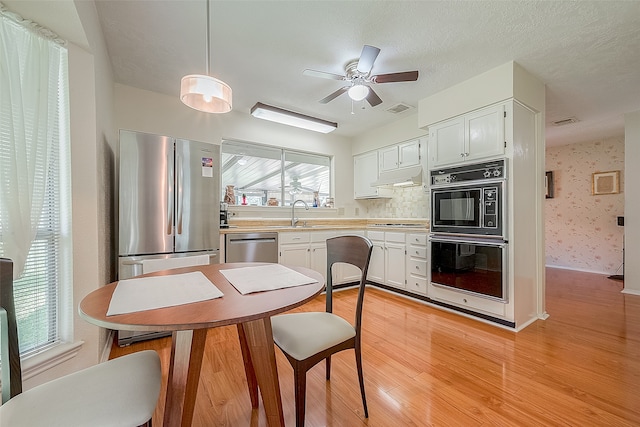 kitchen featuring white cabinetry, ceiling fan, stainless steel appliances, pendant lighting, and light wood-type flooring