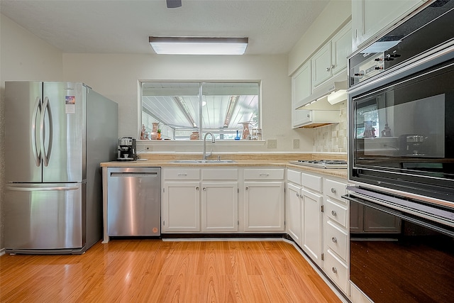 kitchen with appliances with stainless steel finishes, tasteful backsplash, sink, light hardwood / wood-style flooring, and white cabinets