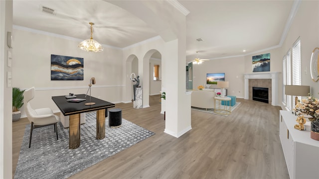 dining area featuring ceiling fan with notable chandelier, light hardwood / wood-style floors, ornamental molding, and a tile fireplace