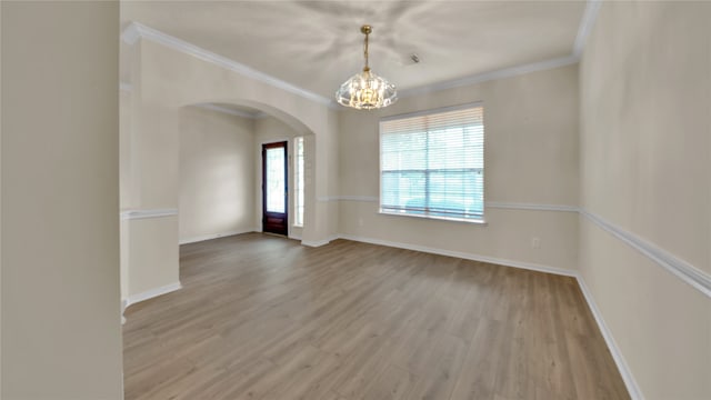 empty room with ornamental molding, wood-type flooring, and a chandelier