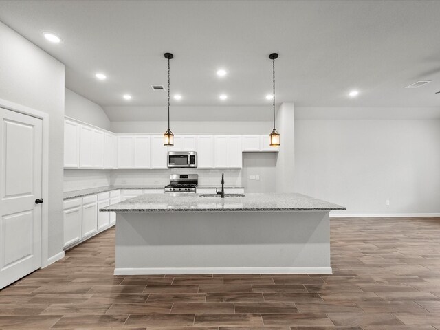 kitchen with light stone counters, an island with sink, sink, white cabinetry, and stainless steel appliances