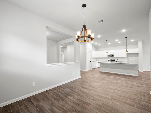 unfurnished living room featuring an inviting chandelier, light wood-type flooring, and sink