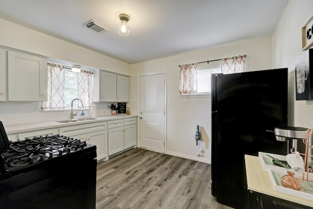 kitchen featuring black appliances, a healthy amount of sunlight, sink, and white cabinets