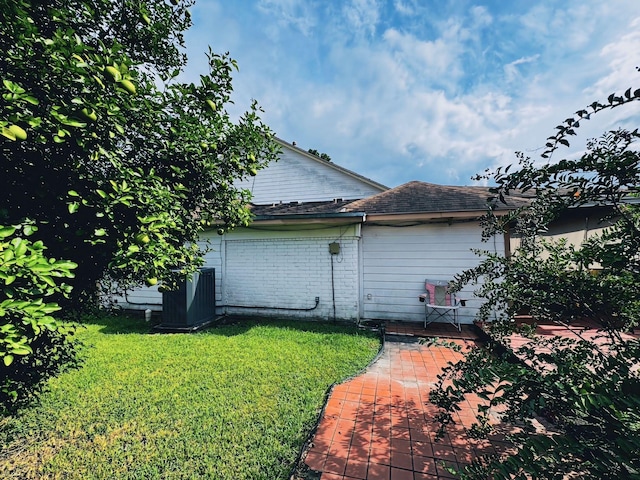 view of home's exterior featuring brick siding, central AC unit, a lawn, and a patio