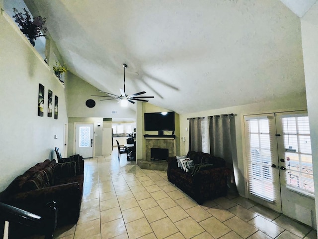 living room featuring plenty of natural light, ceiling fan, a tiled fireplace, and vaulted ceiling