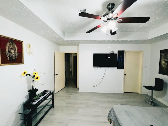 bedroom featuring a textured ceiling, ceiling fan, a tray ceiling, and light hardwood / wood-style floors