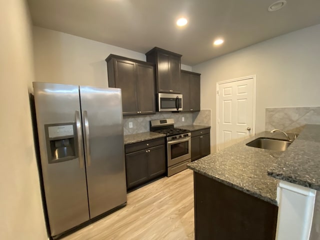 kitchen with light wood-type flooring, backsplash, dark brown cabinets, stainless steel appliances, and sink