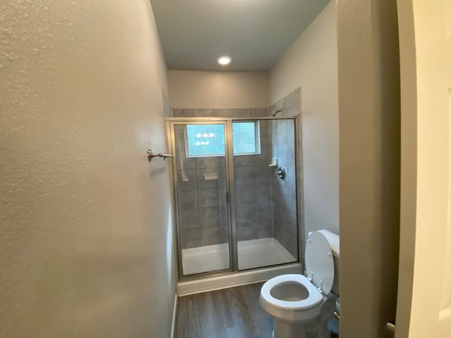 bathroom with wood-type flooring, a shower with shower door, and toilet