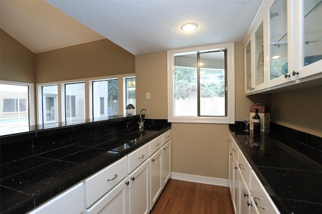 kitchen featuring a textured ceiling, sink, dark wood-type flooring, lofted ceiling, and white cabinets