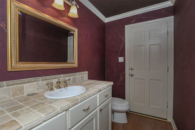 bathroom featuring toilet, ornamental molding, vanity, tasteful backsplash, and wood-type flooring