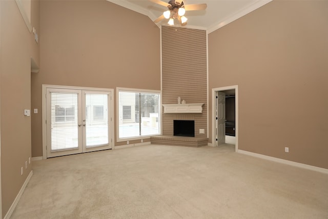 unfurnished living room featuring ornamental molding, a brick fireplace, ceiling fan, a towering ceiling, and light colored carpet