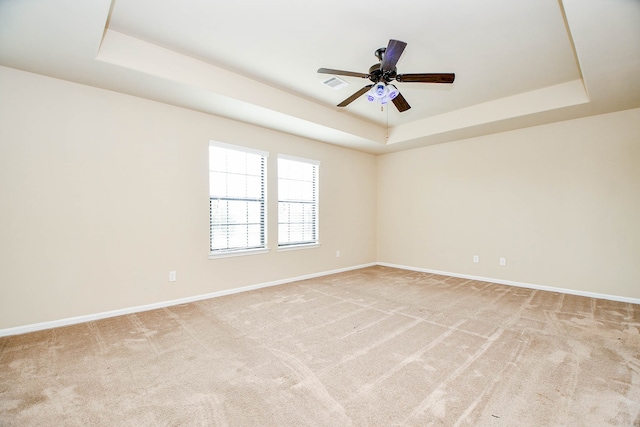 carpeted empty room with a raised ceiling and ceiling fan