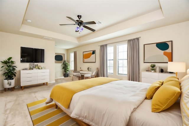 bedroom featuring a raised ceiling, ceiling fan, and light carpet