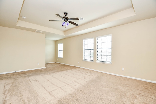 empty room with ceiling fan, a raised ceiling, and light carpet