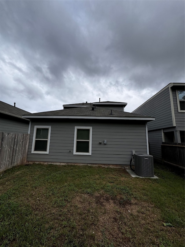 rear view of house featuring central AC unit and a lawn