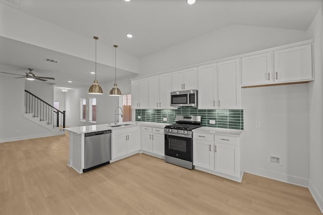 kitchen with appliances with stainless steel finishes, a peninsula, a sink, white cabinetry, and backsplash