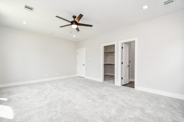 unfurnished bedroom with a closet, ceiling fan, a spacious closet, and carpet floors