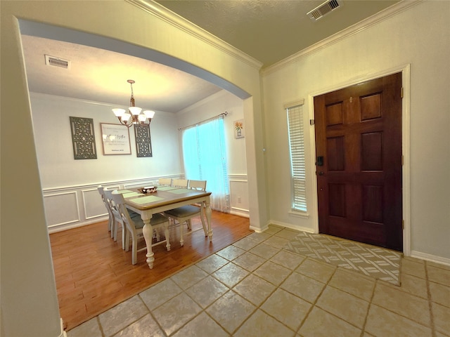 foyer with crown molding, light wood-type flooring, and an inviting chandelier