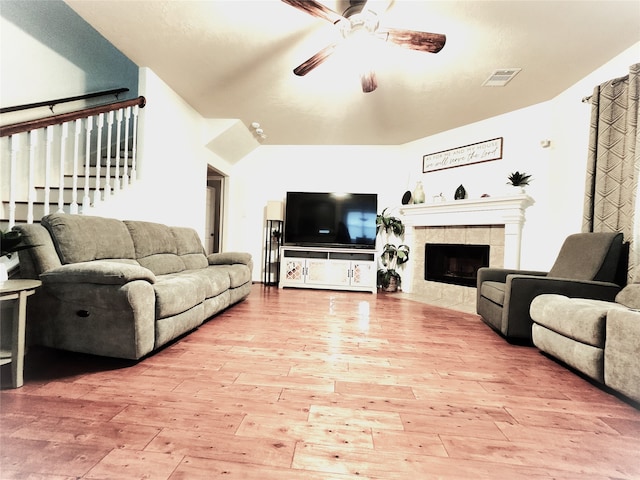 living room featuring lofted ceiling, ceiling fan, a tile fireplace, and light hardwood / wood-style flooring