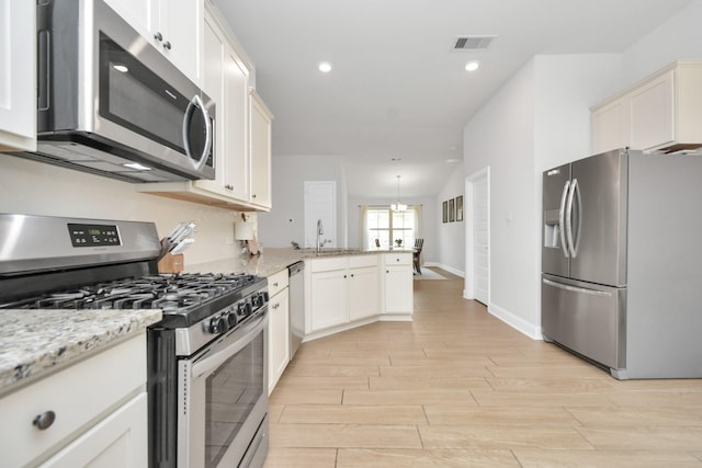 kitchen with kitchen peninsula, stainless steel appliances, hanging light fixtures, light stone countertops, and a chandelier