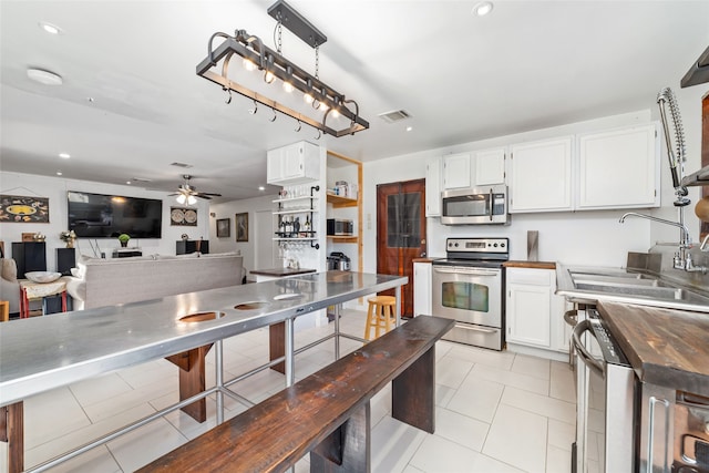 kitchen featuring sink, appliances with stainless steel finishes, decorative light fixtures, white cabinetry, and butcher block counters