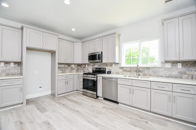 kitchen with light wood-type flooring, tasteful backsplash, stainless steel appliances, and sink